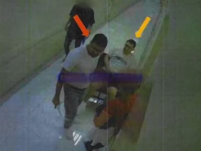 Imagem de câmera de segurança granulada mostrando dois homens suspeitos caminhando por um corredor, com setas coloridas sobrepostas indicando os investigados, still usado em reportagem policial sobre o caso do carro-forte
