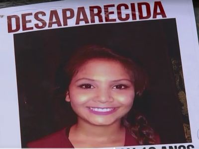 Cartaz de pessoa desaparecida com a foto de uma jovem sorridente, cabelos castanhos, usando blusa vermelha, título DESAPARECIDA em letras grandes vermelhas, cartaz colado em poste, fotografia documental de imprensa